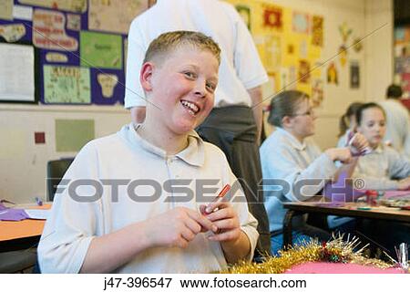 Stock Photo - 12 year old boy, sitting in class, he's coloured pulling a face at camera. Fotosearch