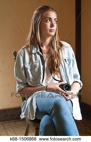 Stock Photo - 15 year old girl sits in an old abandoned house with her camera. Fotosearch
