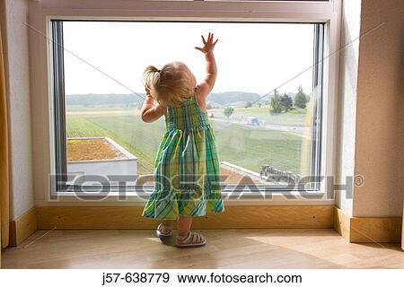 Stock Photo - 16 month old girl playing at a window in a hotel room overlooking a field and highway.. Fotosearch