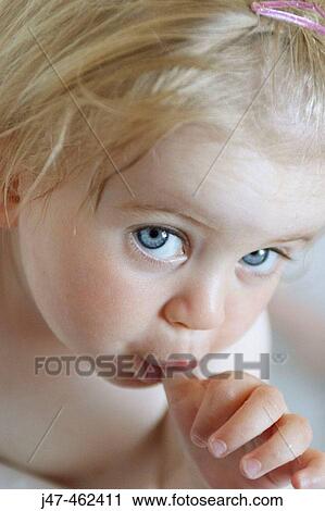 Stock Image - 18 month old baby girl, sucking her thumb, looking directly into the camera. Fotosearch