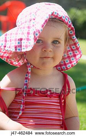 18 month old girl sitting outside wearing a big floppy hat, smiling into camera View Large Photo Image Picture - 18 month old girl sitting outside wearing a big floppy hat, smiling into camera. Fotosearch