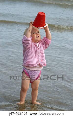 18 month old girl sitting standing on the beach looking into an upturned bucket View Large Photo Image Stock Image - 18 month old girl sitting standing on the beach looking into an upturned bucket. Fotosearch