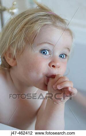 Stock Image - 18 month old girl sucking her thumb and pulling a funny face. Fotosearch
