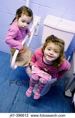 Stock Image - 2, 3 year old girls in a toilet, one of them sitting on the toilet, smiling. Fotosearch