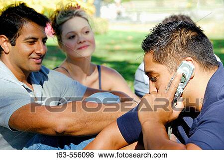 2 male and 1 female young adults sitting in park together- one on cell phone View Large Photo Image Stock Photo - 2 male and 1 female young adults sitting in park together- one on cell phone. Fotosearch
