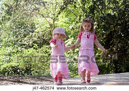 2 sisters, 3 and 1, walking through a park, holding hands, wearing matching dresses View Large Photo Image Picture - 2 sisters, 3 and 1, walking through a park, holding hands, wearing matching dresses. Fotosearch