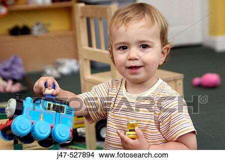 2 year old boy, smiling into camera, holding up a train, playing at nursery View Large Photo Image Picture - 2 year old boy, smiling into camera, holding up a train, playing at nursery. Fotosearch