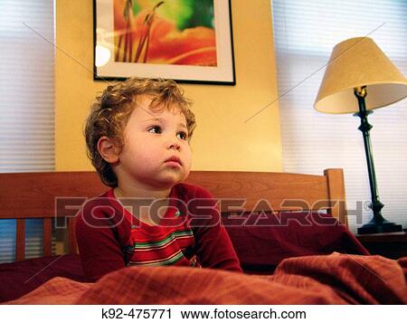 Stock Image - 2-year-old boy watching television in bed. Fotosearch