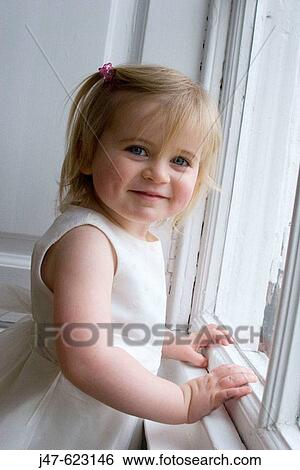 Stock Photograph - 2 year old girl, leaning up against a window smiling into camera. Fotosearch