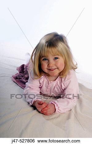 Stock Photograph - 2 year old girl lying on the floor in the studio smiling into camera. Fotosearch