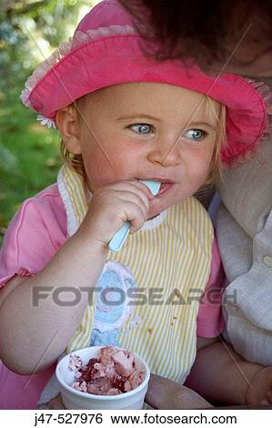 Stock Photograph - 2 year old girl sitting eating icecream, smiling off camera. Fotosearch