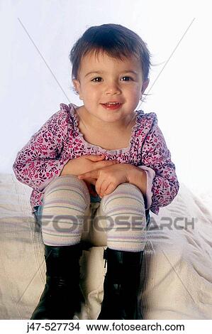 Picture - 2 year old girl sitting on the floor, smiling into camera, studio. Fotosearch
