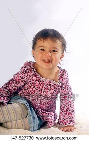 Stock Image - 2 year old girl sitting on the floor, smiling into camera, studio. Fotosearch