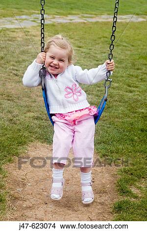 2 year old girl standing at a swing grinning into camera View Large Photo Image Picture - 2 year old girl standing at a swing grinning into camera. Fotosearch