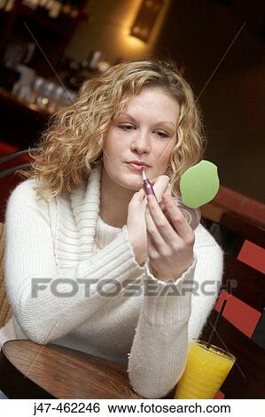 20 year old girl sitting in a bar with a glass of orange, applying lipstick in a little mirror View Large Photo Image Stock Photograph - 20 year old girl sitting in a bar with a glass of orange, applying lipstick in a little mirror. Fotosearch