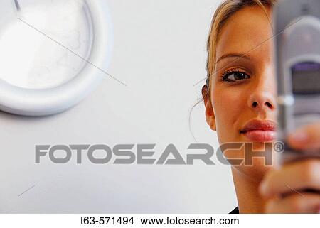 20 yr old woman holding cell phone in office/home with clock on wall View Large Photo Image Picture - 20 yr old woman holding cell phone in office/home with clock on wall. Fotosearch