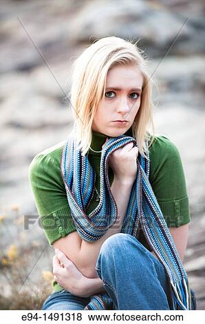 Stock Photo - 21 year old blond woman wearing green sweater and blue jeans sitting on a rock formation in the mountains.. Fotosearch