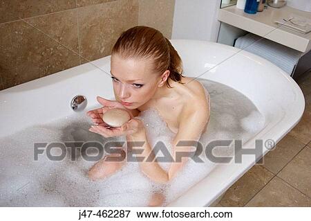 Stock Photo - 21 year old girl in the bath, holding a bar of soap smelling it. Fotosearch