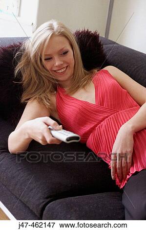 21 year old girl lying on sofa smiling at tv, holding the remote control View Large Photo Image Stock Photo - 21 year old girl lying on sofa smiling at tv, holding the remote control. Fotosearch