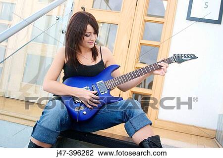 Stock Image - 21 year old girl, sitting on staircase, holding a bright blue electric guitar, smiling. Fotosearch