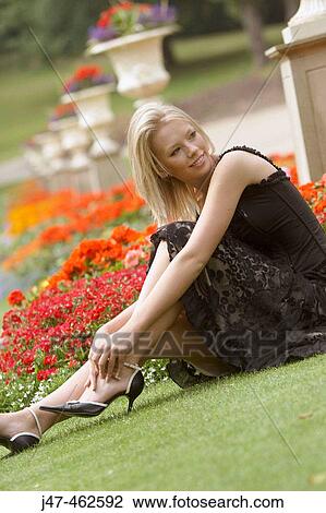 Stock Image - 21 year old girl sitting on the grass, looking off camera, smiling. Fotosearch