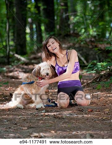 Stock Image - 23 year old brunette woman dressed in exercise clothing walking her dog through a forest. Fotosearch