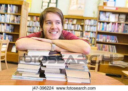 24 year old man leaning on a pile of books, smiling, in the library View Large Photo Image Picture - 24 year old man leaning on a pile of books, smiling, in the library. Fotosearch
