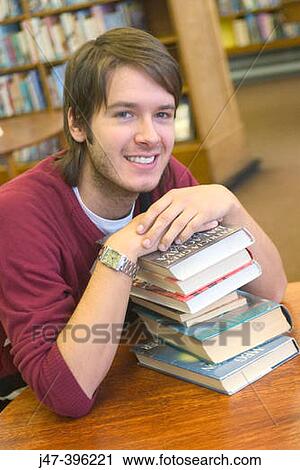 24 year old man leaning on a pile of books, smiling, in the library View Large Photo Image Stock Image - 24 year old man leaning on a pile of books, smiling, in the library. Fotosearch