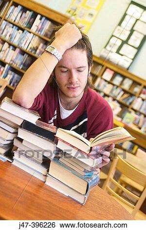 24 year old man, reading a book, resting on a huge pile of books, head in hand, in the library View Large Photo Image Stock Photograph - 24 year old man, reading a book, resting on a huge pile of books, head in hand, in the library. Fotosearch