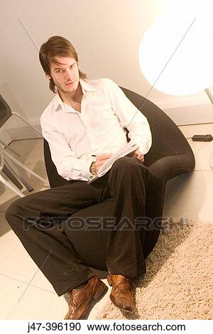 Stock Image - 24 year old man sitting in chair writing looking into camera full lengh. Fotosearch