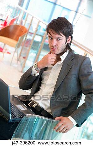 Stock Image - 24 year old man sitting in chair, serious expression hand on chin. Fotosearch