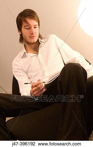 Stock Image - 24 year old man sitting in chair writing. Fotosearch