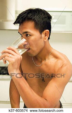 25-30 y/o Asian man in kitchen drinking water View Large Photo Image Picture - 25-30 y/o Asian man in kitchen drinking water. Fotosearch