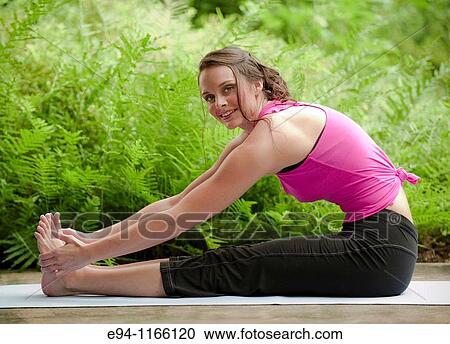 Stock Image - 25 year old brunette woman in a garden settng wearing work out clothing, stretching and exercising looking at the camera.. Fotosearch