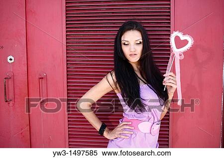 Stock Photography - 25 year old woman outdoors with pink heart against industrial metal red door. Fotosearch