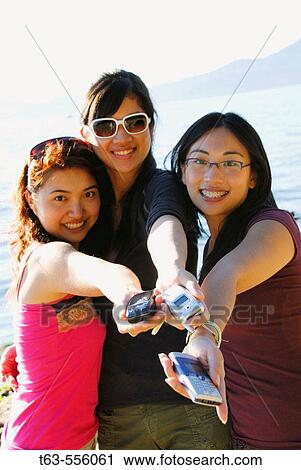3 asian women holding cell phones out in hands View Large Photo Image Stock Image - 3 asian women holding cell phones out in hands. Fotosearch