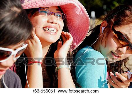 Stock Image - 3 asian women sitting together on beach listening to music. Fotosearch