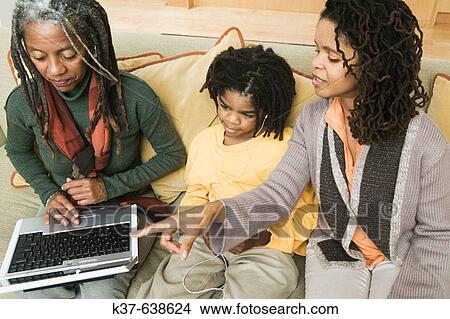 3 generations of African American family at home, with grandma using laptop being advised by older daughter & her grandson listening to his ipod. View Large Photo Image Picture - 3 generations of African American family at home, with grandma using laptop being advised by older daughter & her grandson listening to his ipod.. Fotosearch
