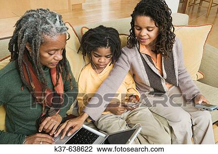 3 generations of African American family at home, with grandma using laptop being advised by older daughter & her grandson listening to his ipod View Large Photo Image Stock Image - 3 generations of African American family at home, with grandma using laptop being advised by older daughter & her grandson listening to his ipod. Fotosearch