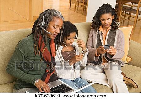 Stock Photo - 3 generations of African American family at home using various technologies including ipod, laptop, blackberry.. Fotosearch