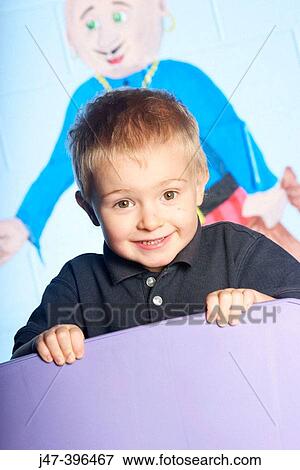 Stock Photo - 3 year old boy leaning over the back of a chair, looking into camera, excited. Fotosearch