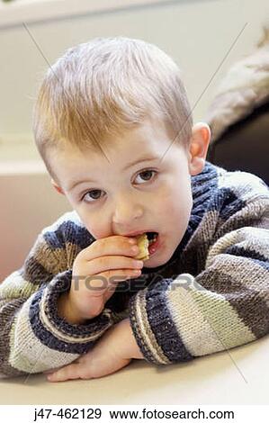 Stock Photo - 3 year old boy sitting eating a biscuit. Fotosearch