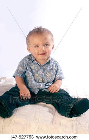 Stock Image - 3 year old boy smiling into camera, sitting on his bottom. Fotosearch