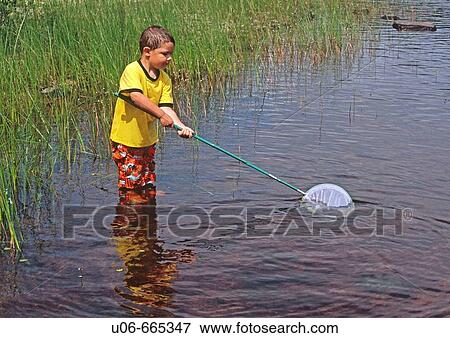 Stock Photo - 3 year old boy trying to dip fish in a lake. Fotosearch