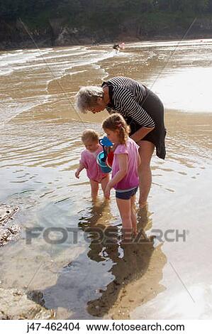 3 year old girl and 18 month old baby girl, with their nanny on the beach looking at their finds in the bucket View Large Photo Image Picture - 3 year old girl and 18 month old baby girl, with their nanny on the beach looking at their finds in the bucket. Fotosearch