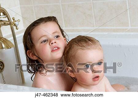 Stock Photo - 3 year old girl and 18 month old baby girl, in the bath, looking off camera. Fotosearch