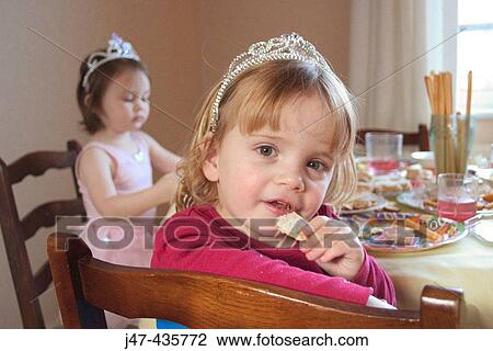 Stock Image - 3 year old girl at a party, smiling into camera, eating. Fotosearch
