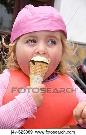 Stock Photo - 3 year old girl eating an icecream, looking off camera.. Fotosearch