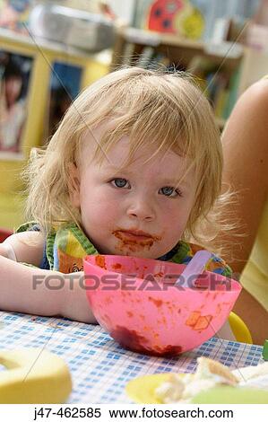Stock Photography - 3 year old girl eating her dinner at nursery, her face covered in food. Fotosearch