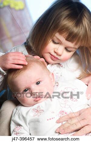 Stock Photo - 3 year old girl holding her 8 week old baby sister. Fotosearch